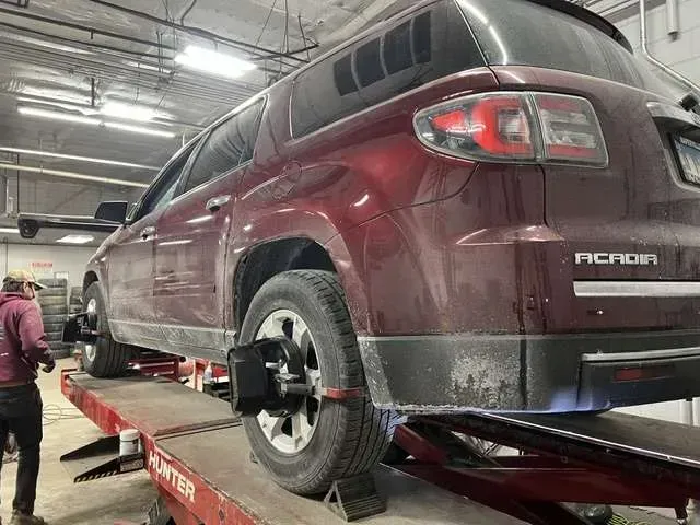 Maroon SUV on a car lift with alignment equipment in a garage. Mechanic stands nearby.