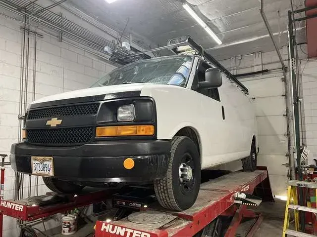White van on a red lift inside a garage. The van has a black front and a license plate.