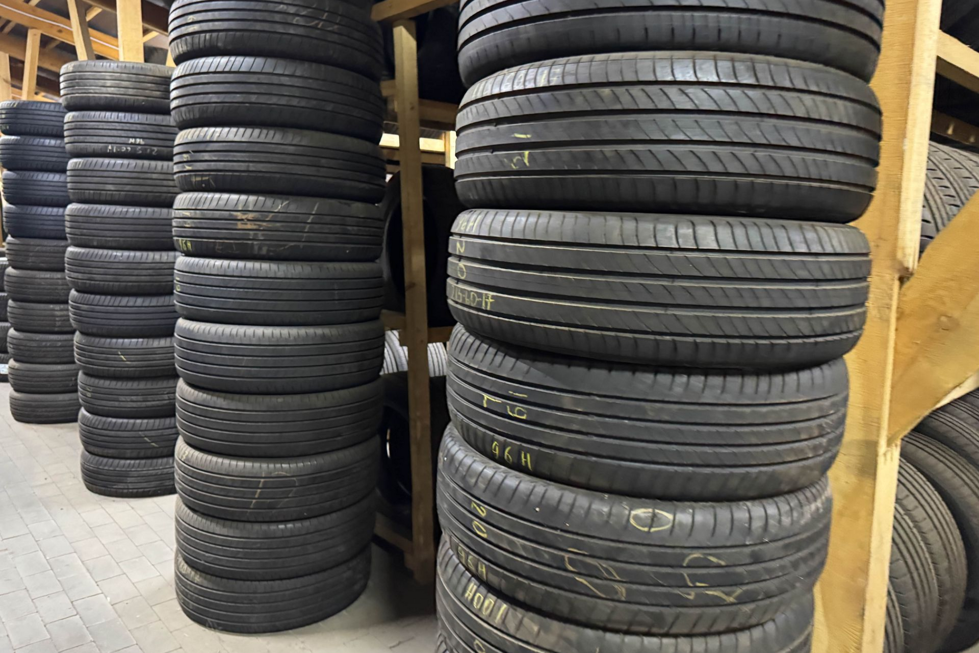 Tires stacked in rows within a wooden storage rack. Dark rubber with visible treads.