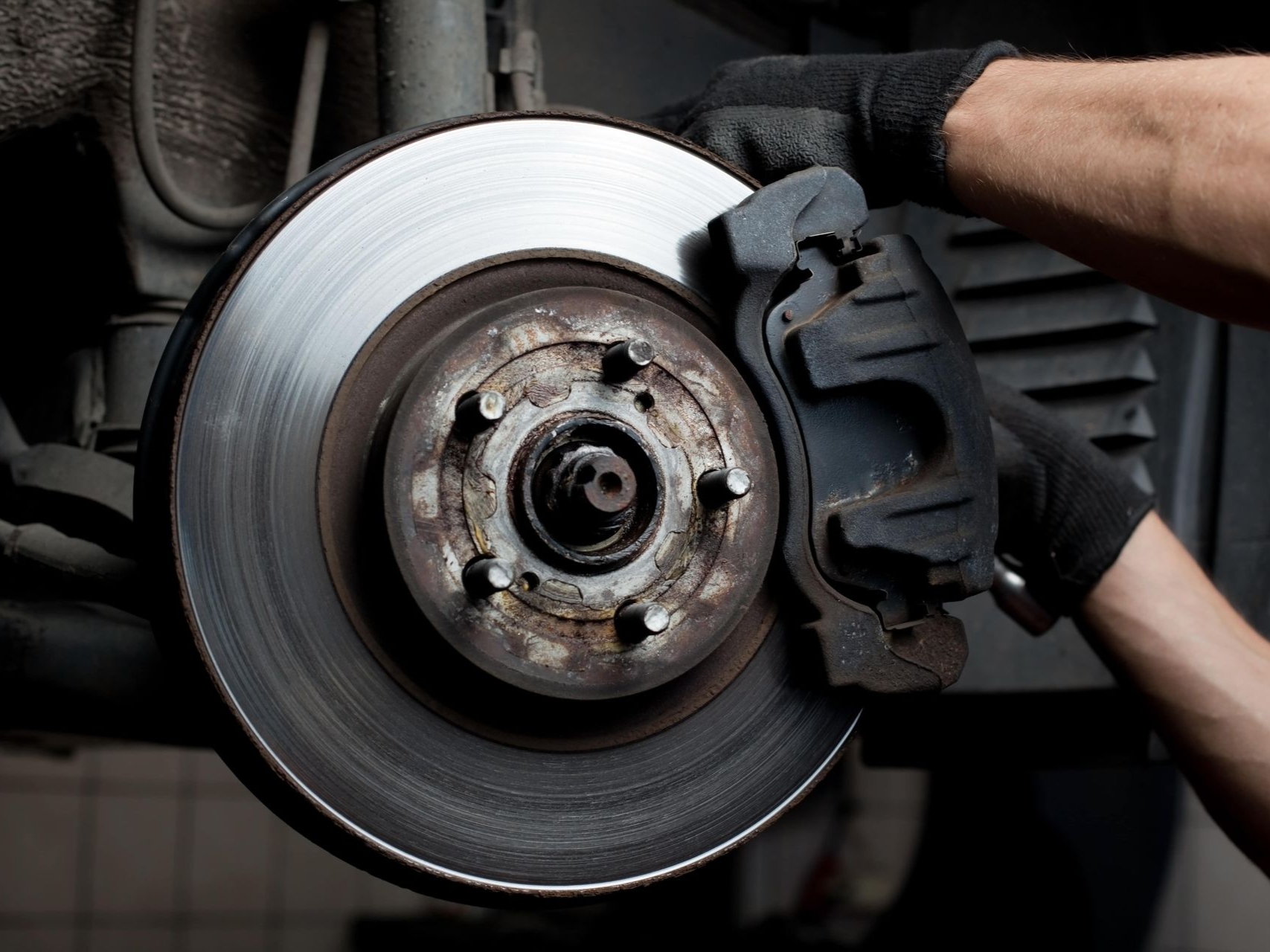 Person in black gloves working on car brake disc.