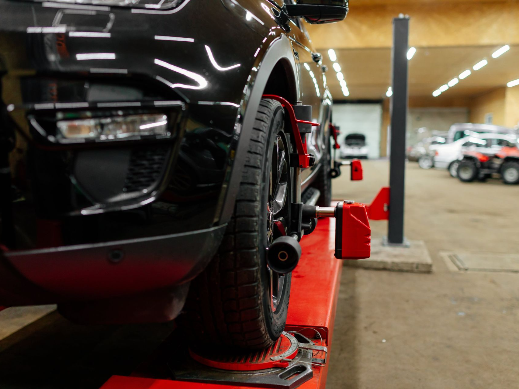 Black car being aligned on a red lift in an auto shop. Wheel alignment equipment attached to the tire.