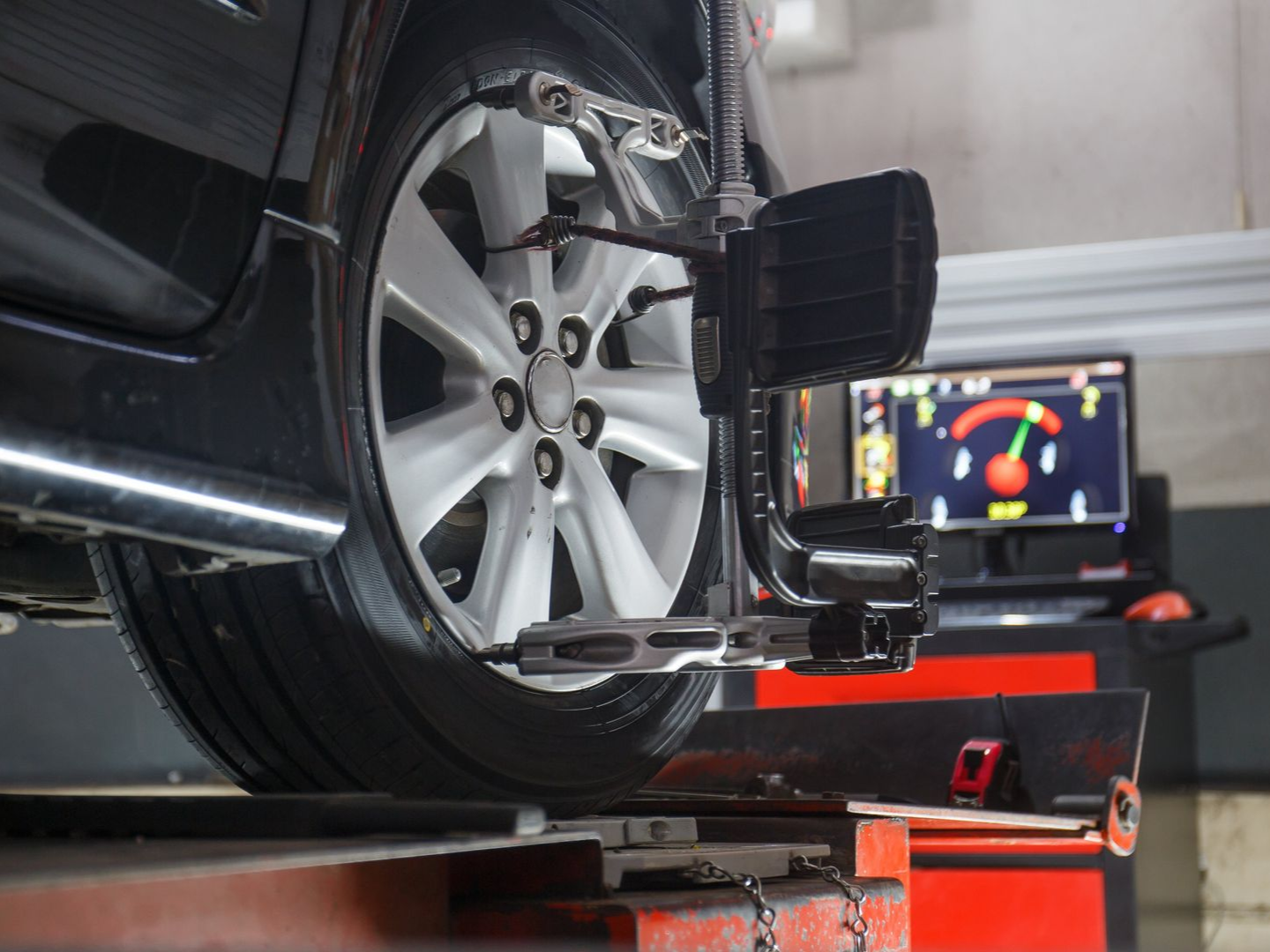 Car wheel on alignment machine in a garage. Computer monitor displays readings.