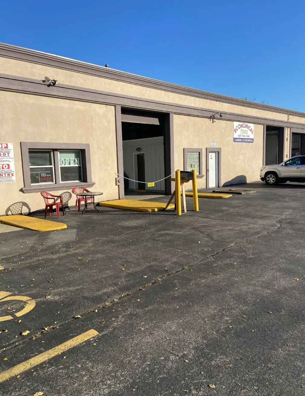 Exterior of a tan building with an open garage bay, outdoor seating, and a parked vehicle.