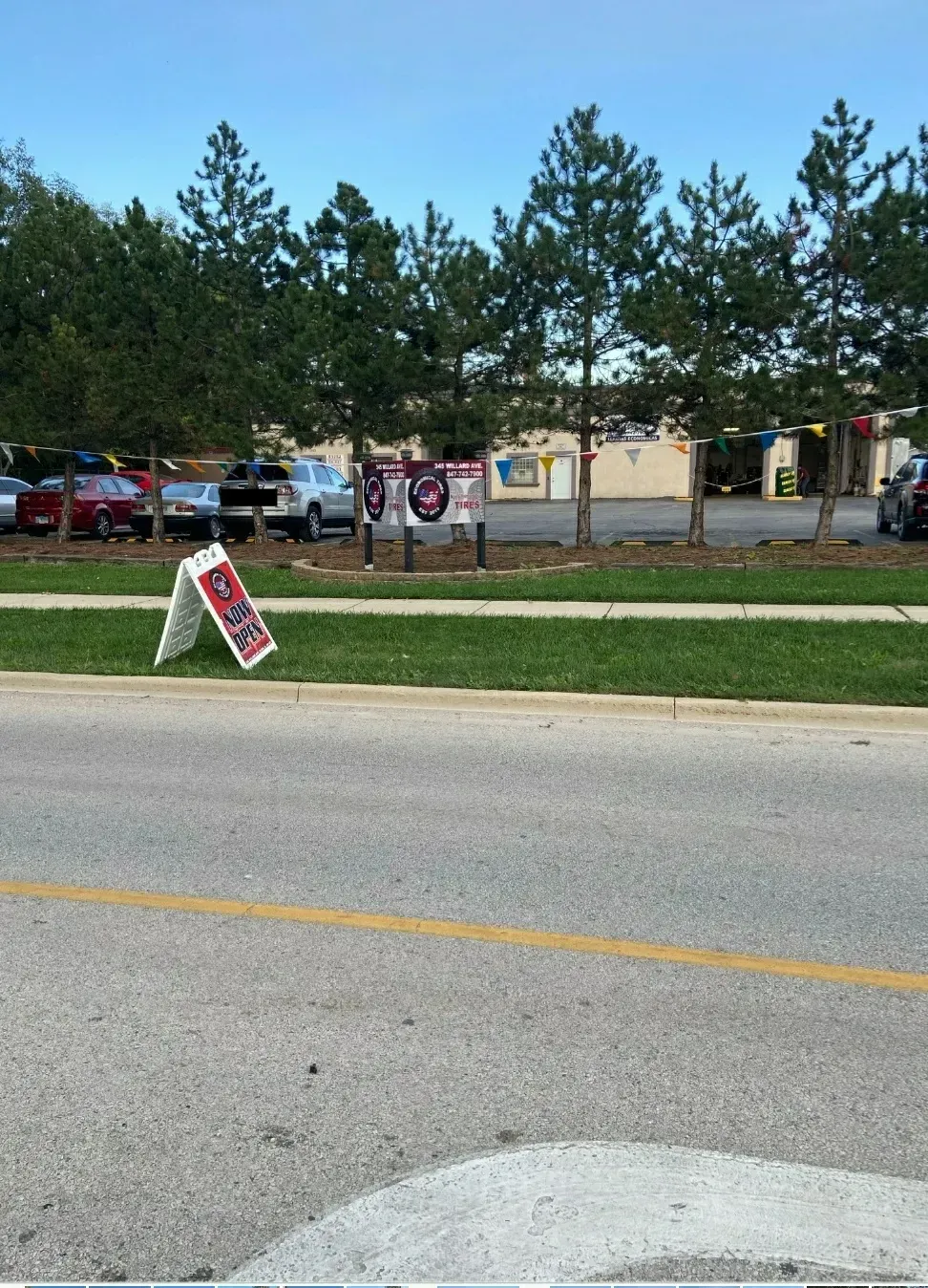 An A-frame sign on a grassy median, trees and a parking lot in the background.