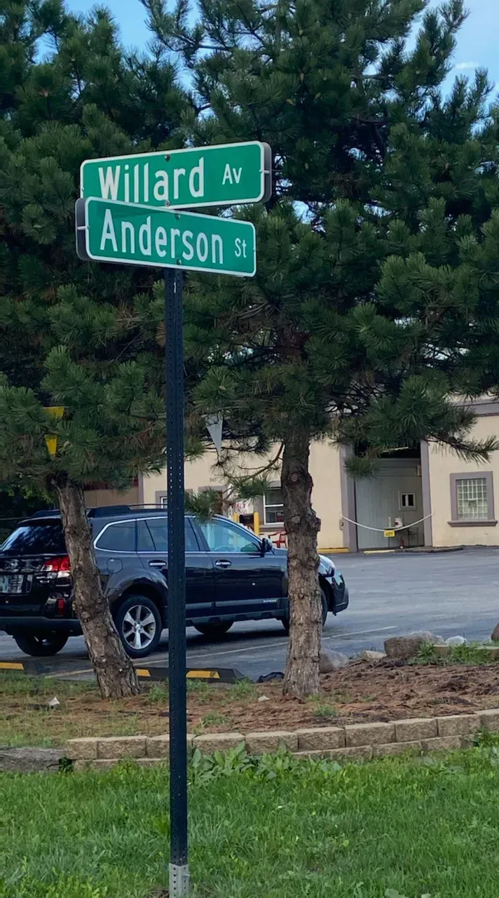 Street sign: Willard Ave, Anderson St, with parked SUV and building in background.