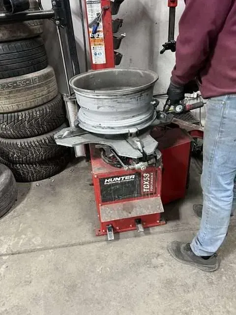 A mechanic using a Hunter tire machine to work on a silver car rim in a garage.