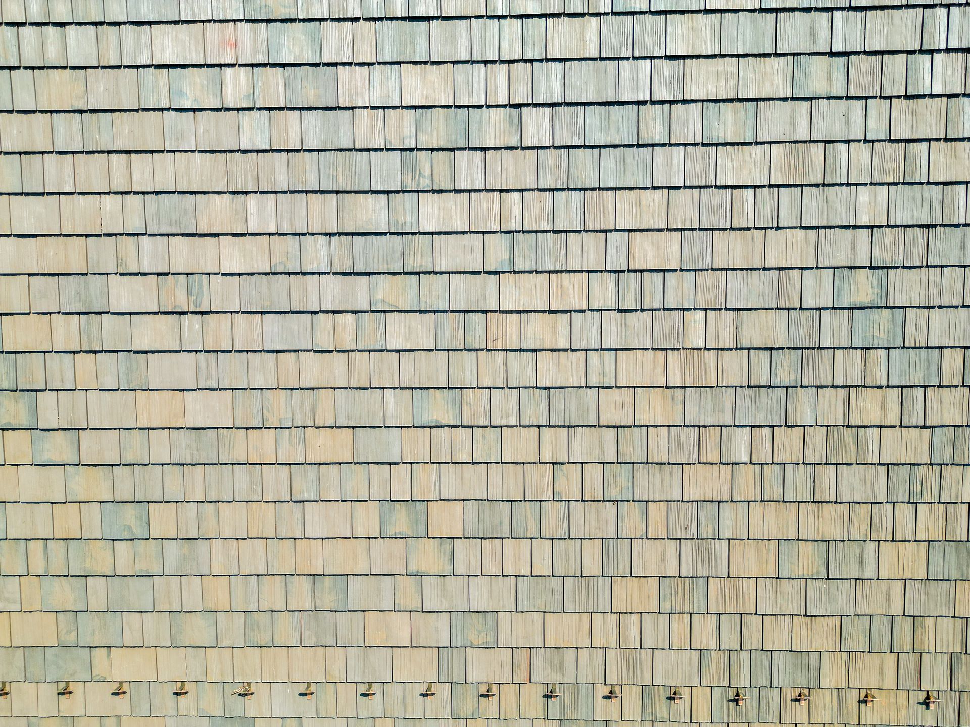 Close-up of a weathered wooden shingle wall in faded gray, beige, and blue tones.