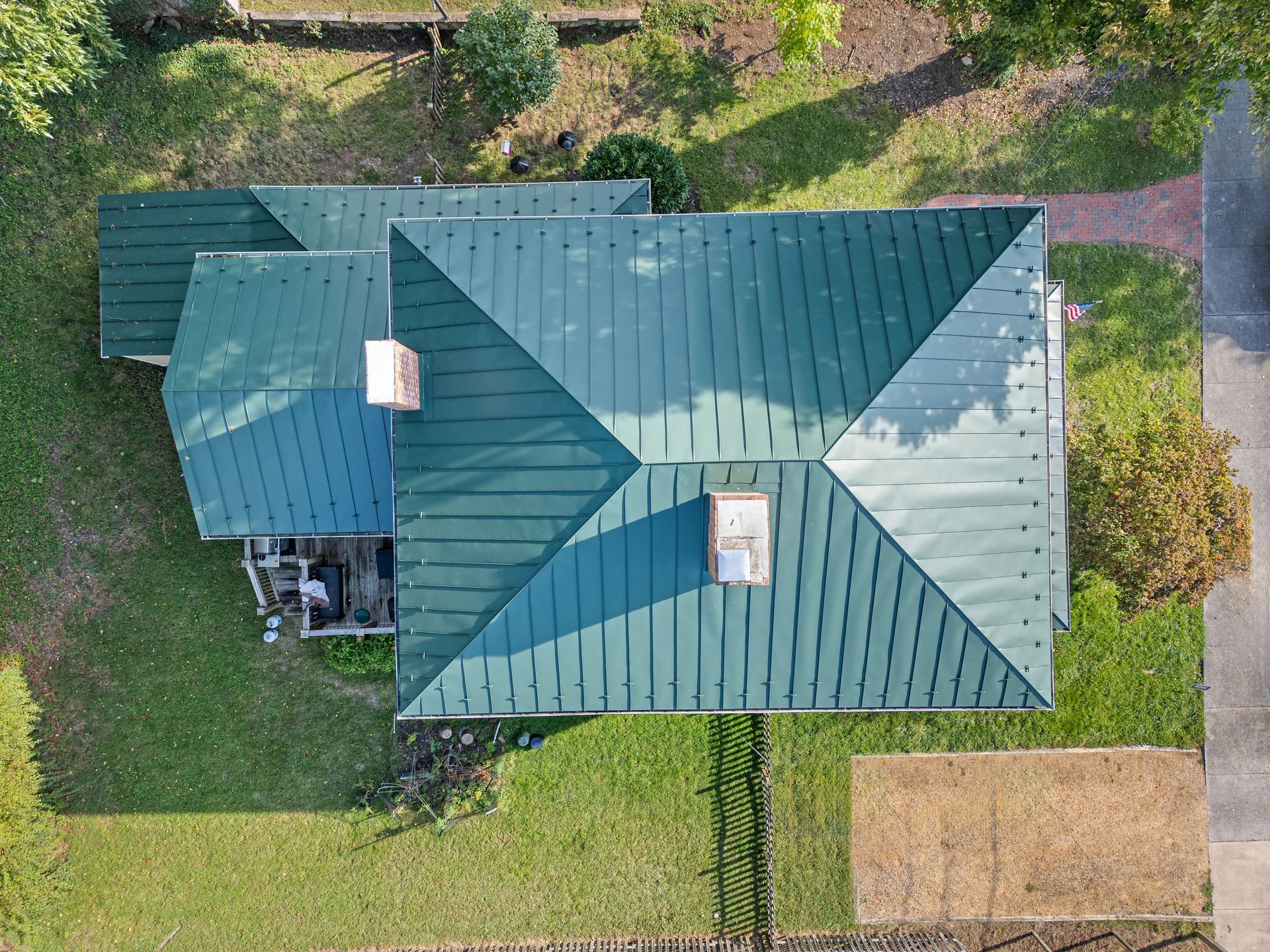 Aerial view of a house with a green metal roof and surrounding lawn and trees.