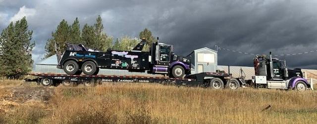 A tow truck is sitting on top of a flatbed trailer in a field.