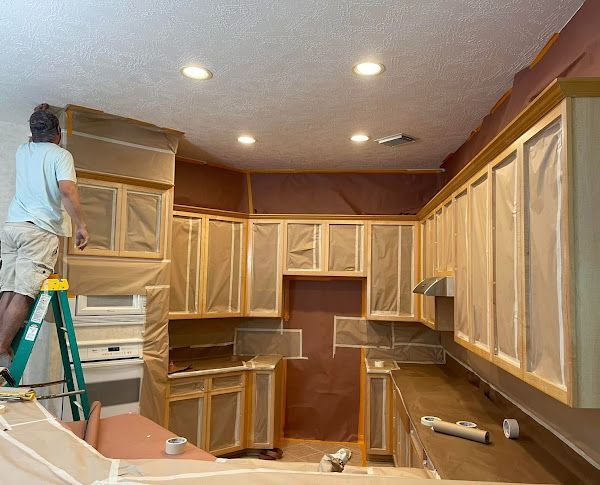 A man is standing on a ladder in a kitchen painting cabinets.