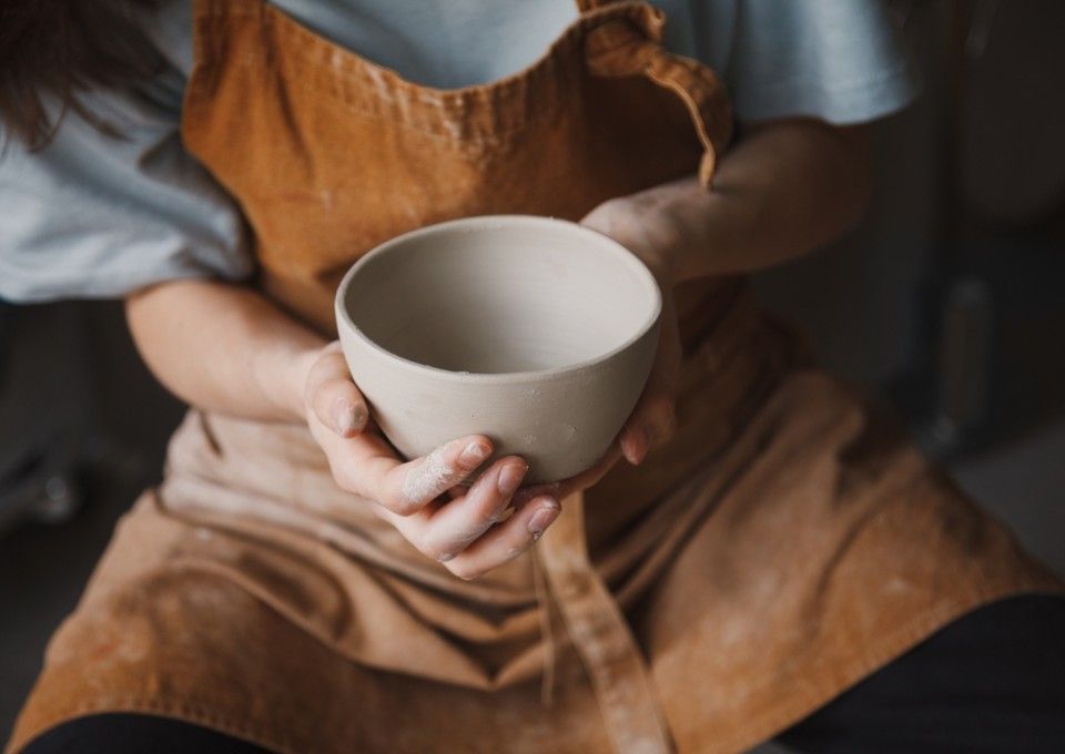A person wearing a brown apron holds a plain, light-colored ceramic bowl with both hands.