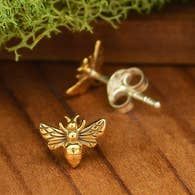A pair of bee stud earrings are sitting on a wooden table.