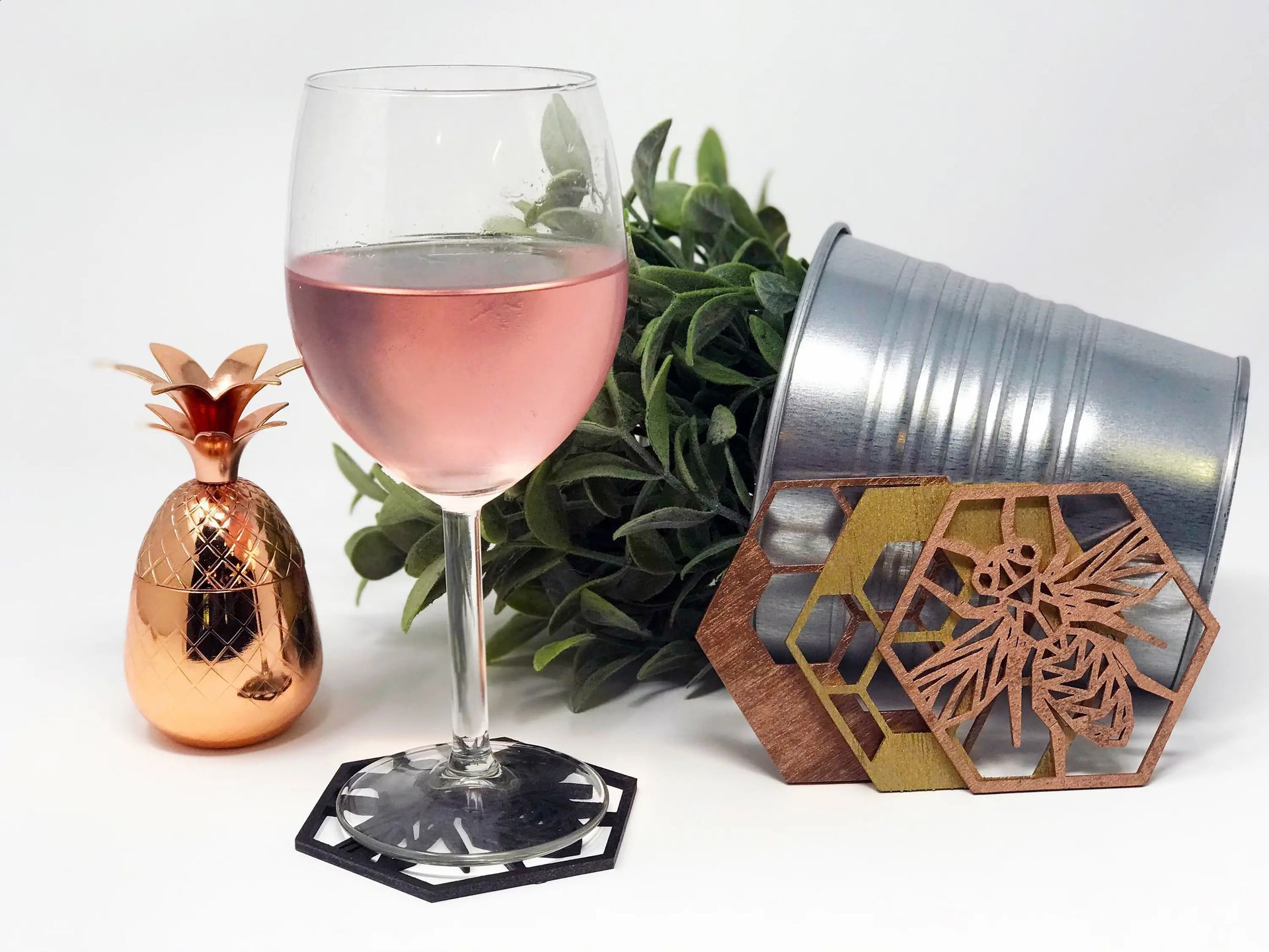 A glass of wine is sitting on a coaster next to a pineapple and a bucket.