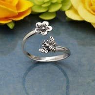 A silver ring with a bee and a flower on it is sitting on a table.