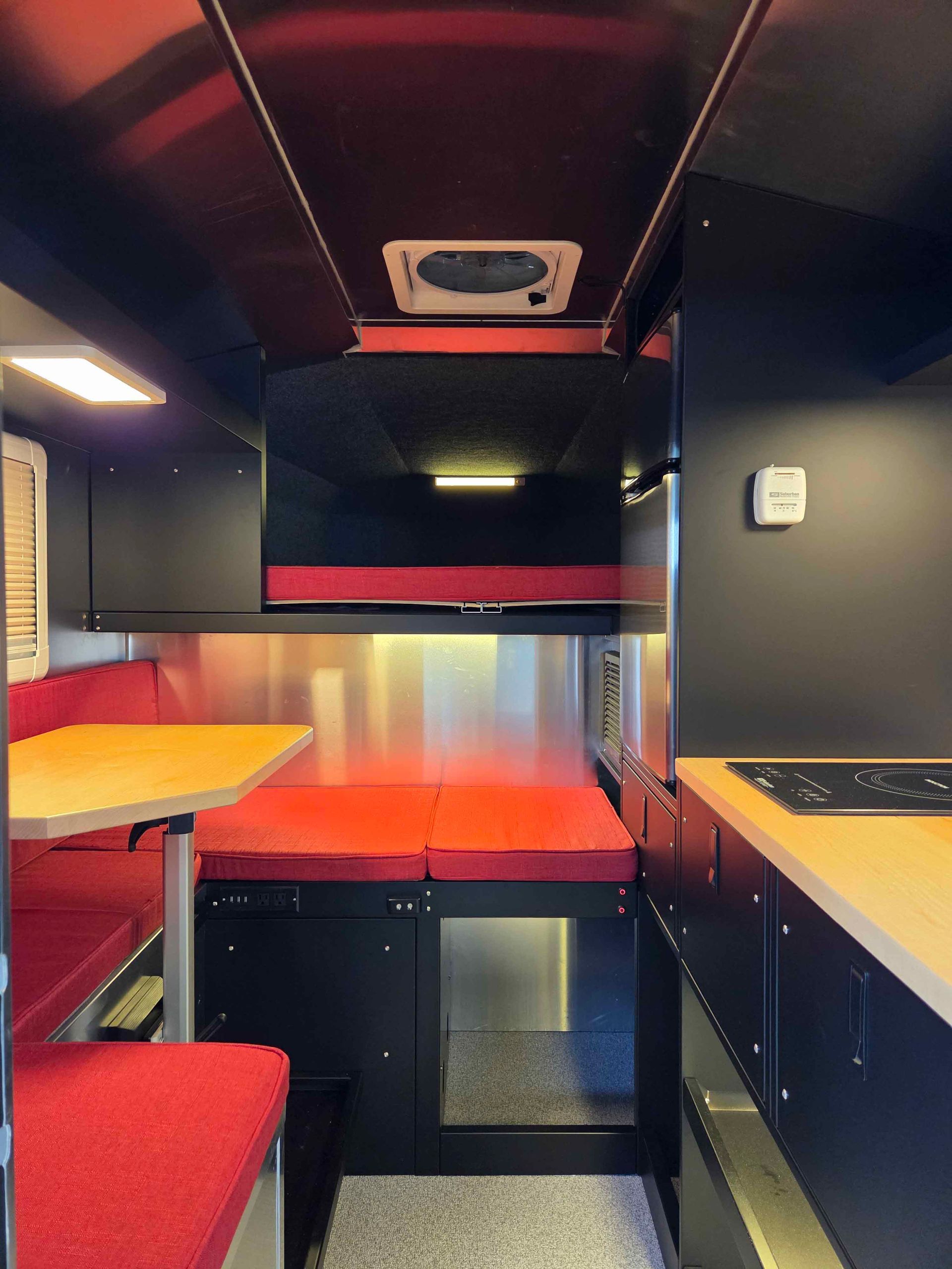 Interior view of a camper van with red seating, black cabinets, and a mounted TV.