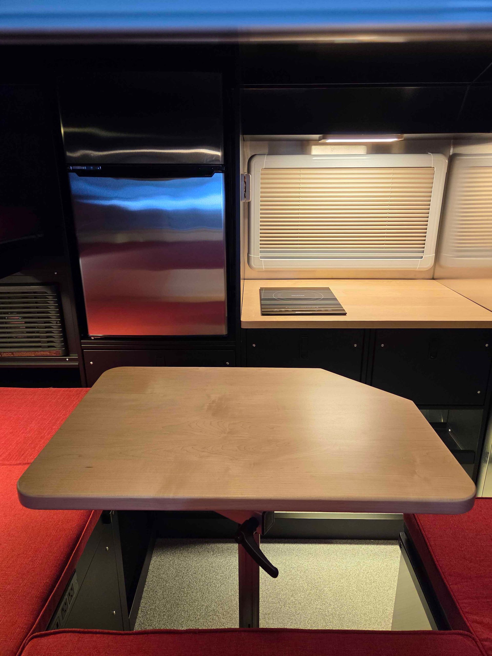 A small wooden table with a red couch in a van, next to a fridge and countertop.