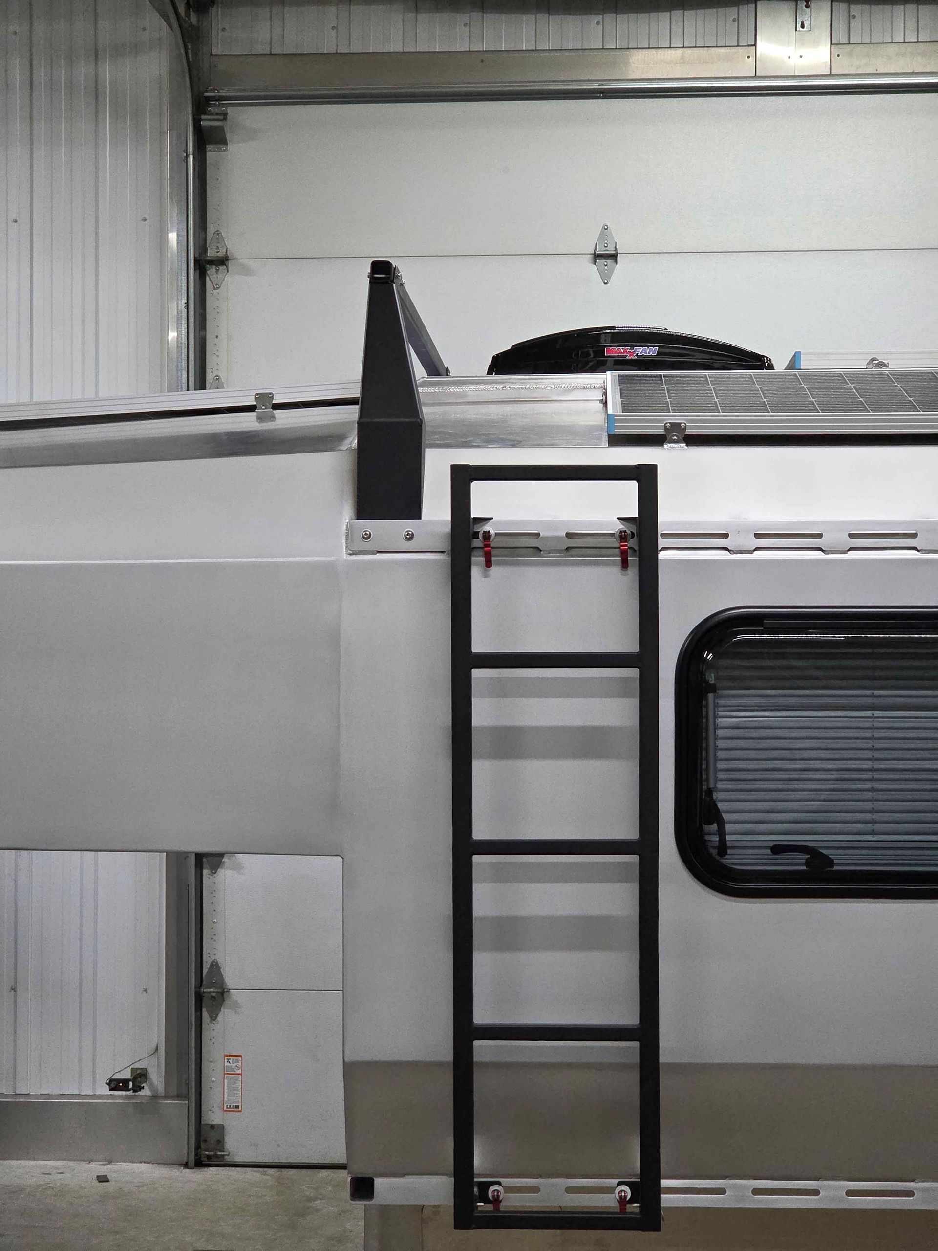 Black ladder on the side of a white camper van, leading to the roof.