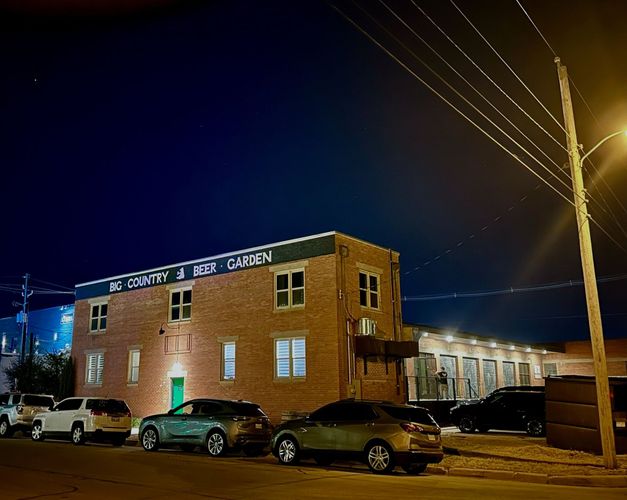 A row of cars are parked in front of a large brick building at night.