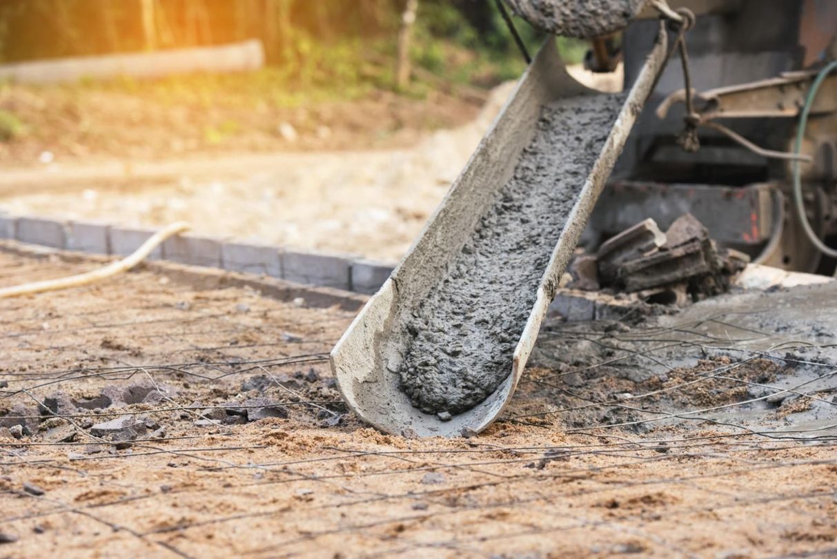 Concrete pouring from a mixer onto prepared ground at a construction site.