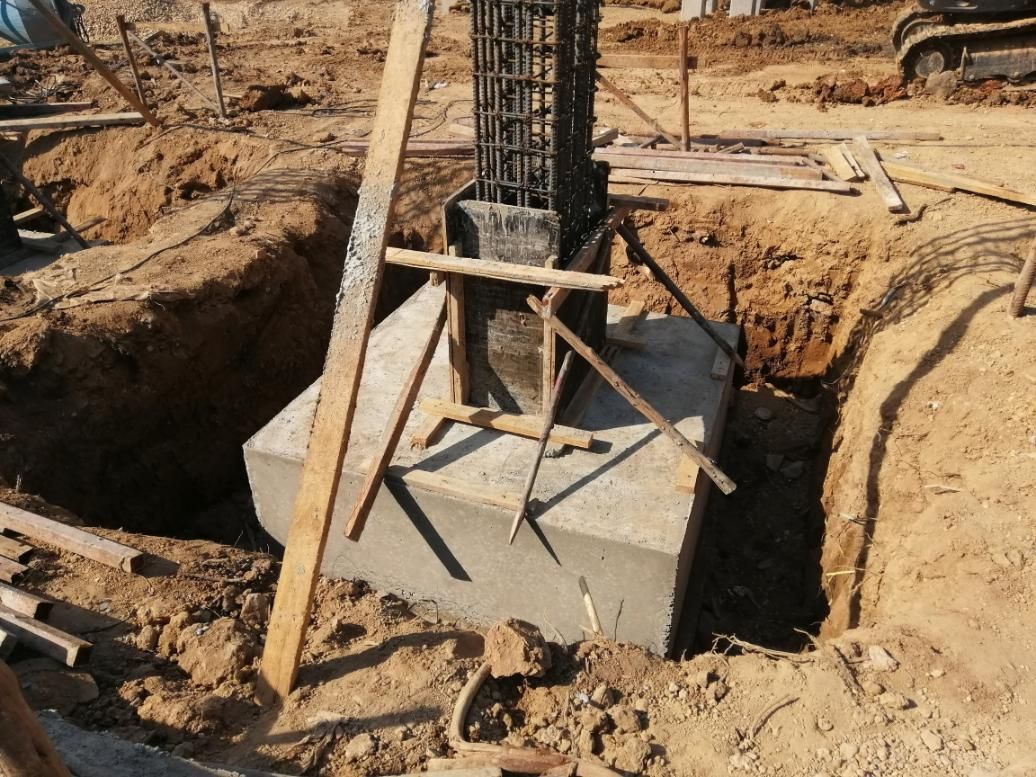 Foundation base with concrete pillar in a construction site, surrounded by dirt.