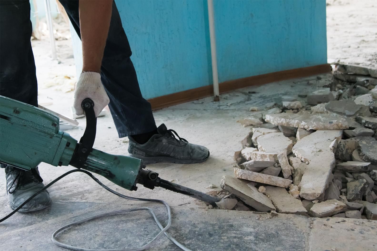 Person using a jackhammer to break up concrete floor; construction site setting.