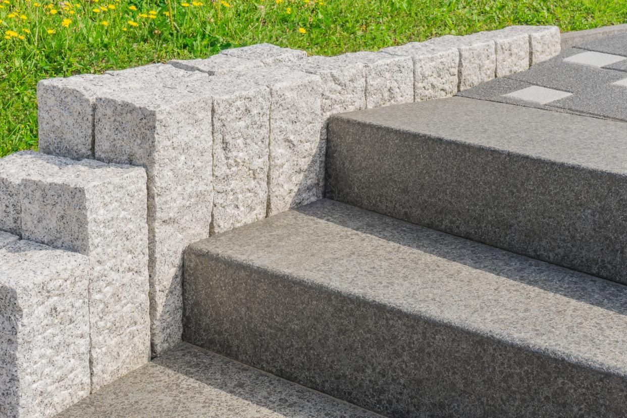 Stone steps with a textured retaining wall next to green grass.