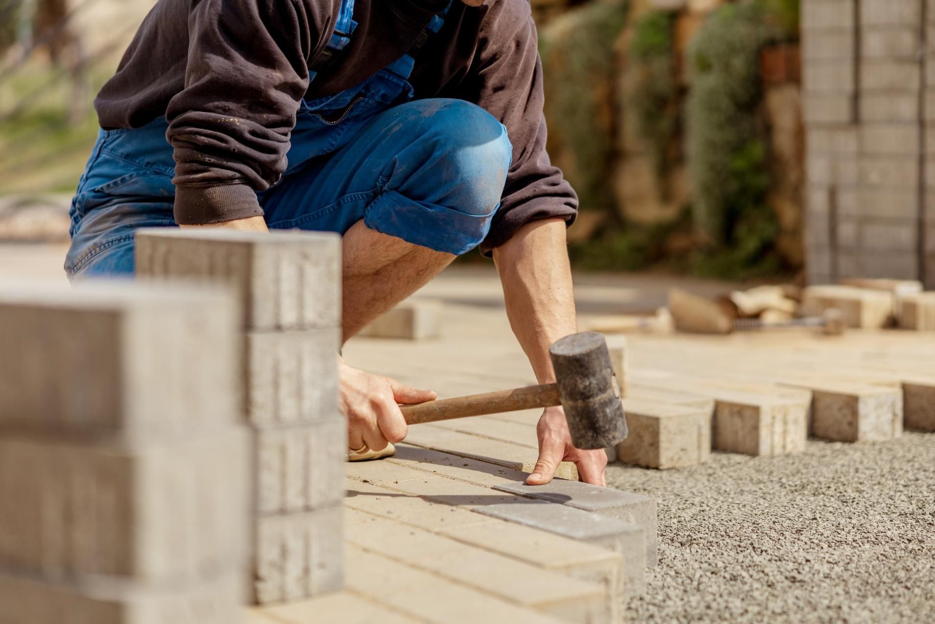 Man laying paving stones, using a mallet to adjust them outdoors.