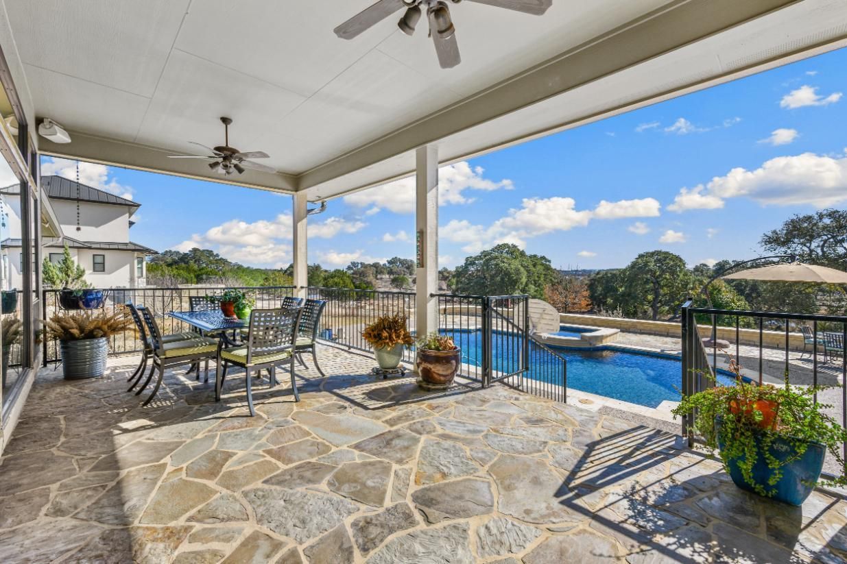 Covered patio with stone floor, table, pool, and scenic view on a sunny day.
