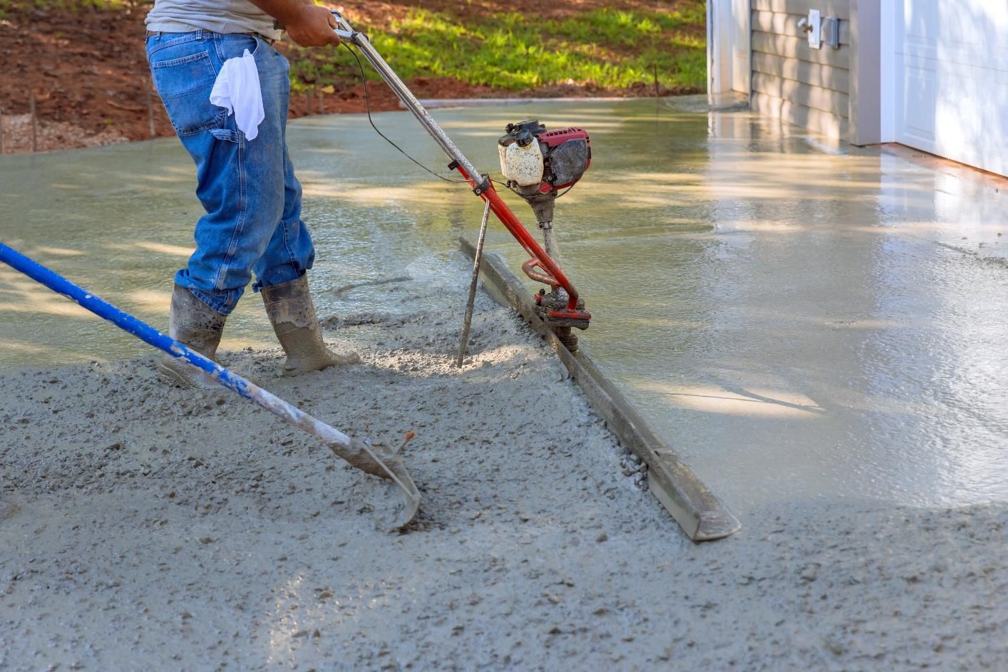 Person leveling wet concrete with a power screed on a construction site.