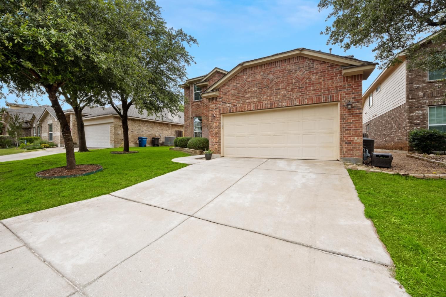 Two-story brick house with beige garage door, concrete driveway, and green lawn on a sunny day.
