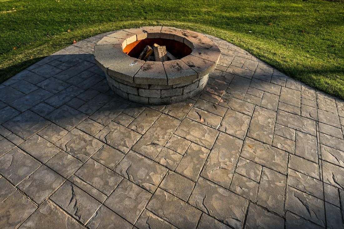 Fire pit on a stone patio with a backdrop of green grass.