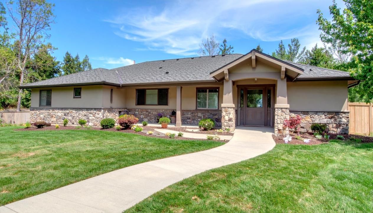 Tan ranch-style house with stone accents, a curving sidewalk, and a grassy yard on a sunny day.