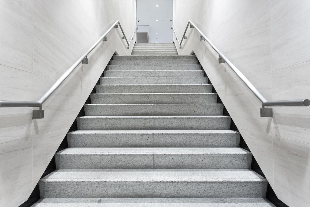Staircase with stone steps, metal handrails, and white walls.