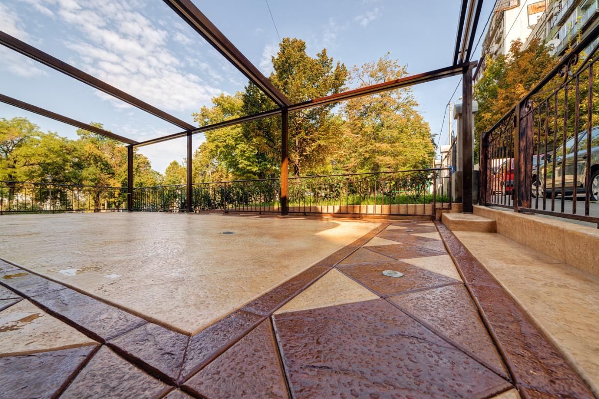 Patio with geometric tile design and metal frame. Trees and sky visible in the background.