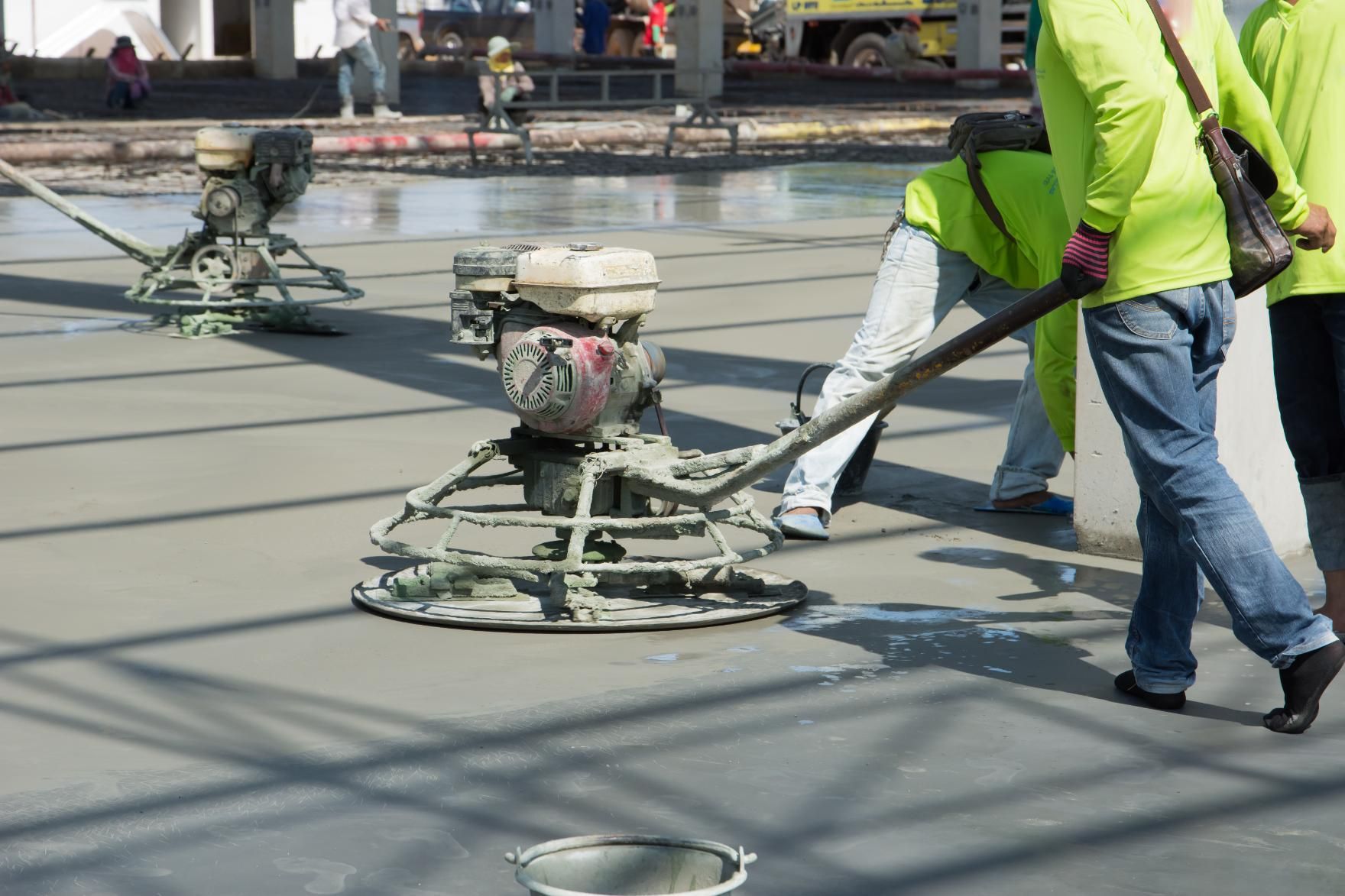 Construction workers smoothing wet concrete with power trowels outdoors.