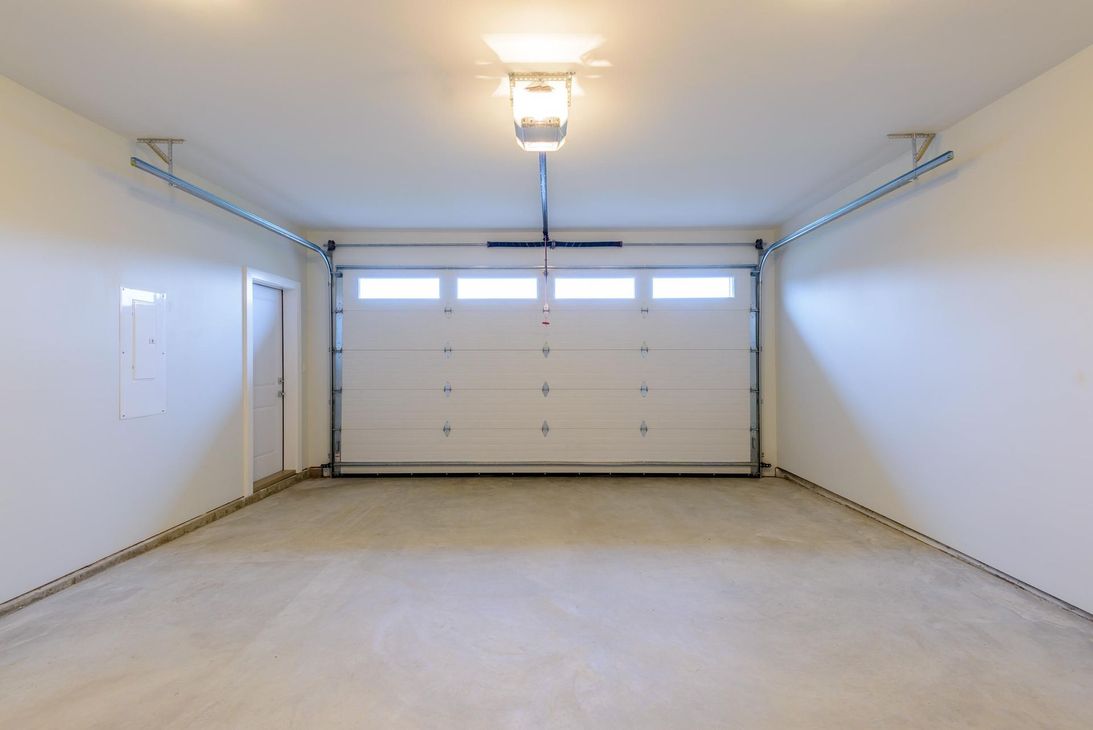 Empty, white garage with a closed door, garage door, and concrete floor.