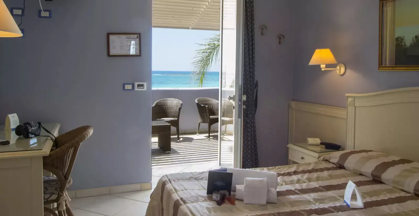 Camera da letto con balcone vista mare; letto, scrivania e sedie in una stanza con pareti blu.