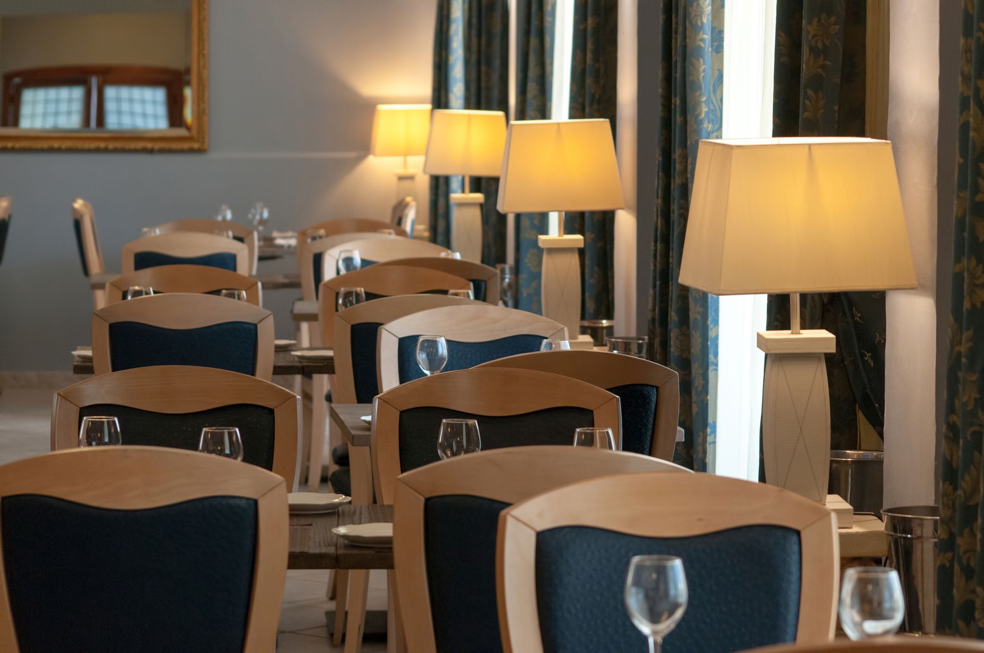 Restaurant dining room with rows of tables, chairs, and lamps.