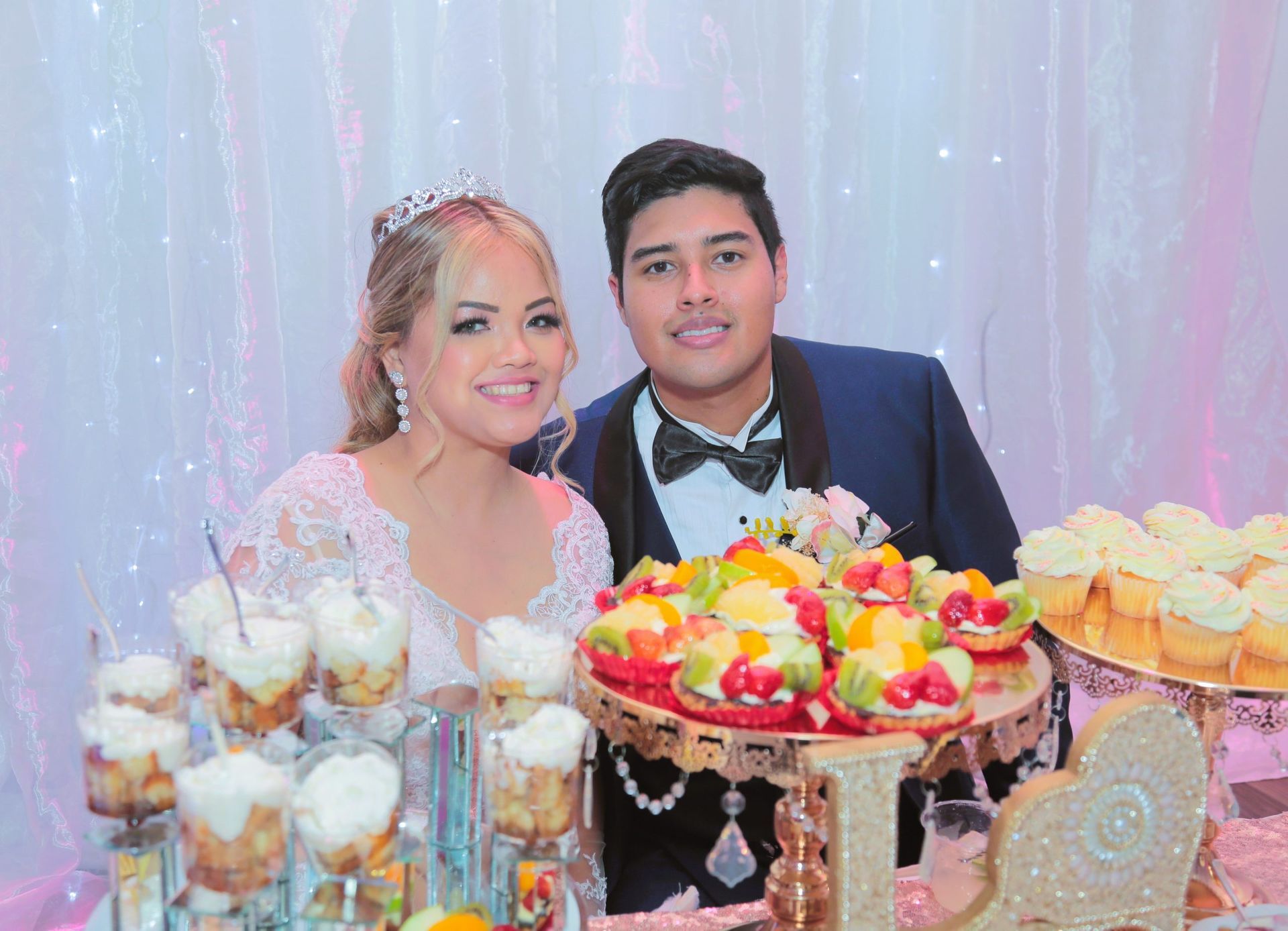 A bride and groom are posing for a picture in front of a dessert table.