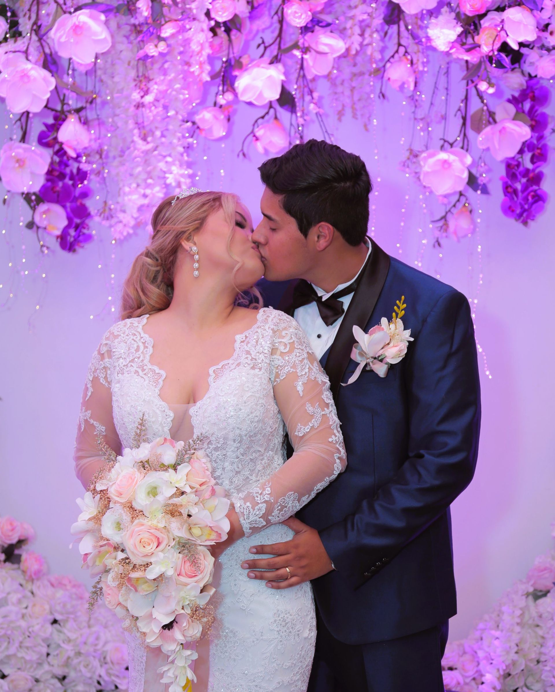 A bride and groom kissing in front of purple flowers