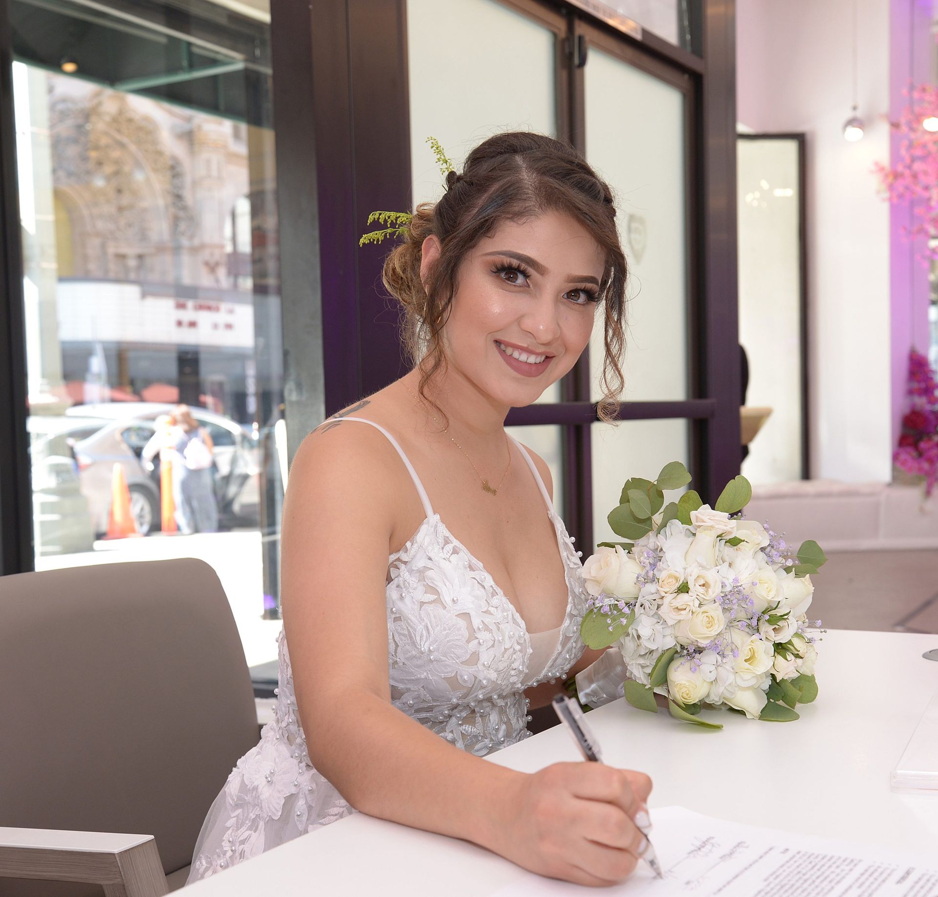 A woman in a wedding dress is sitting at a table with a bouquet of flowers.