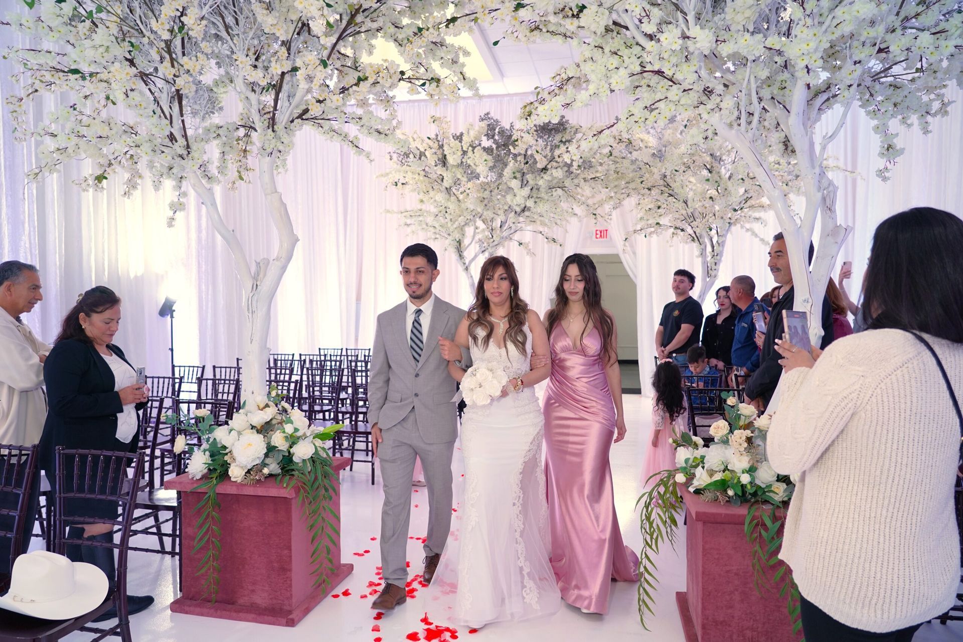 A woman is taking a picture of a bride and groom walking down the aisle at a wedding.