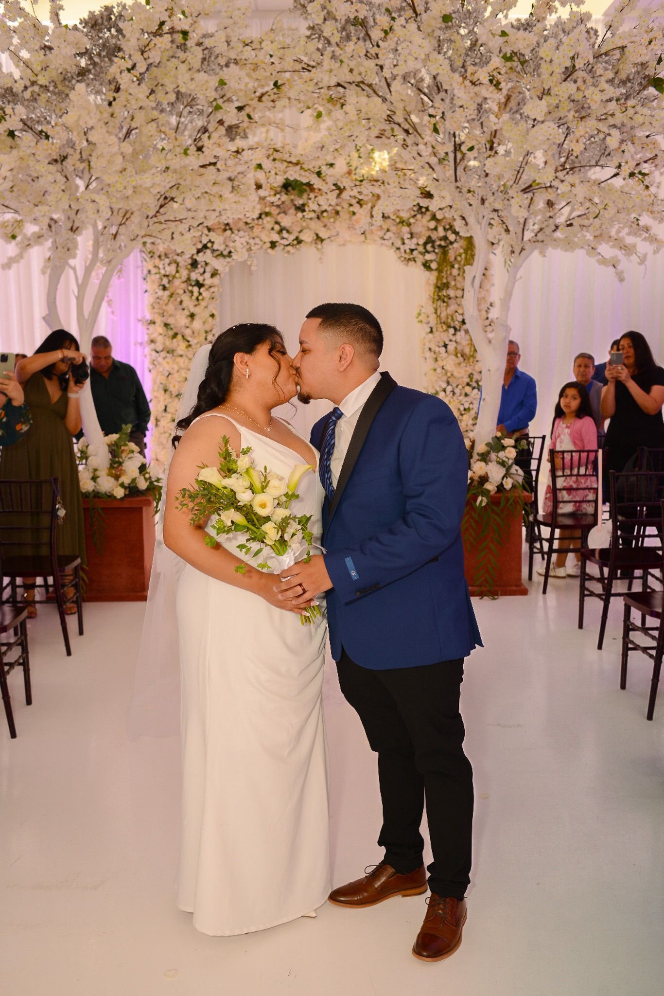 A bride and groom kissing under a floral arch at their wedding ceremony.