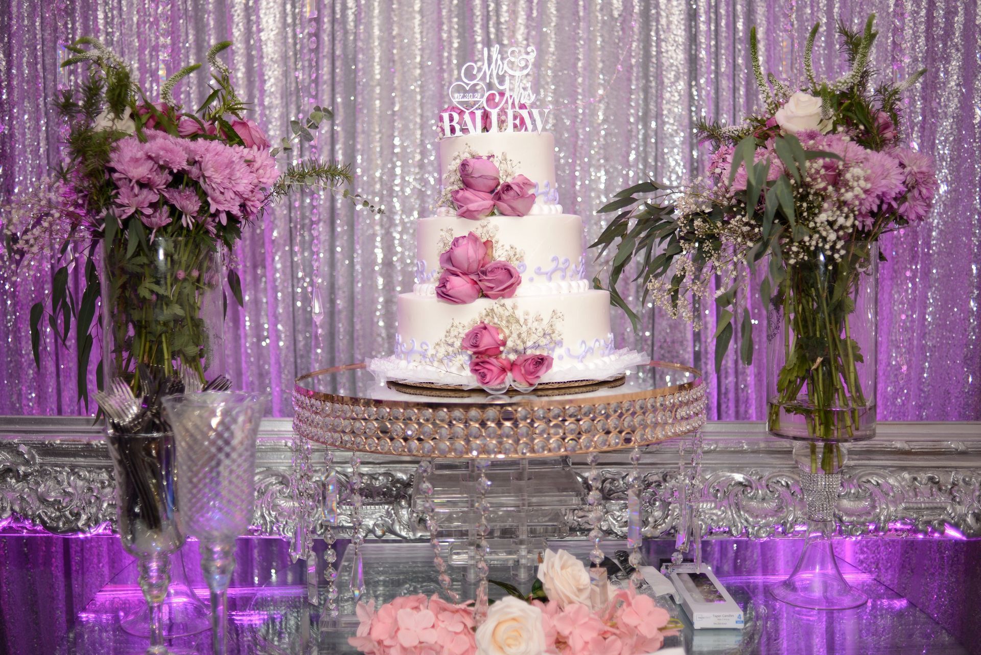 A wedding cake is sitting on top of a glass table surrounded by flowers.