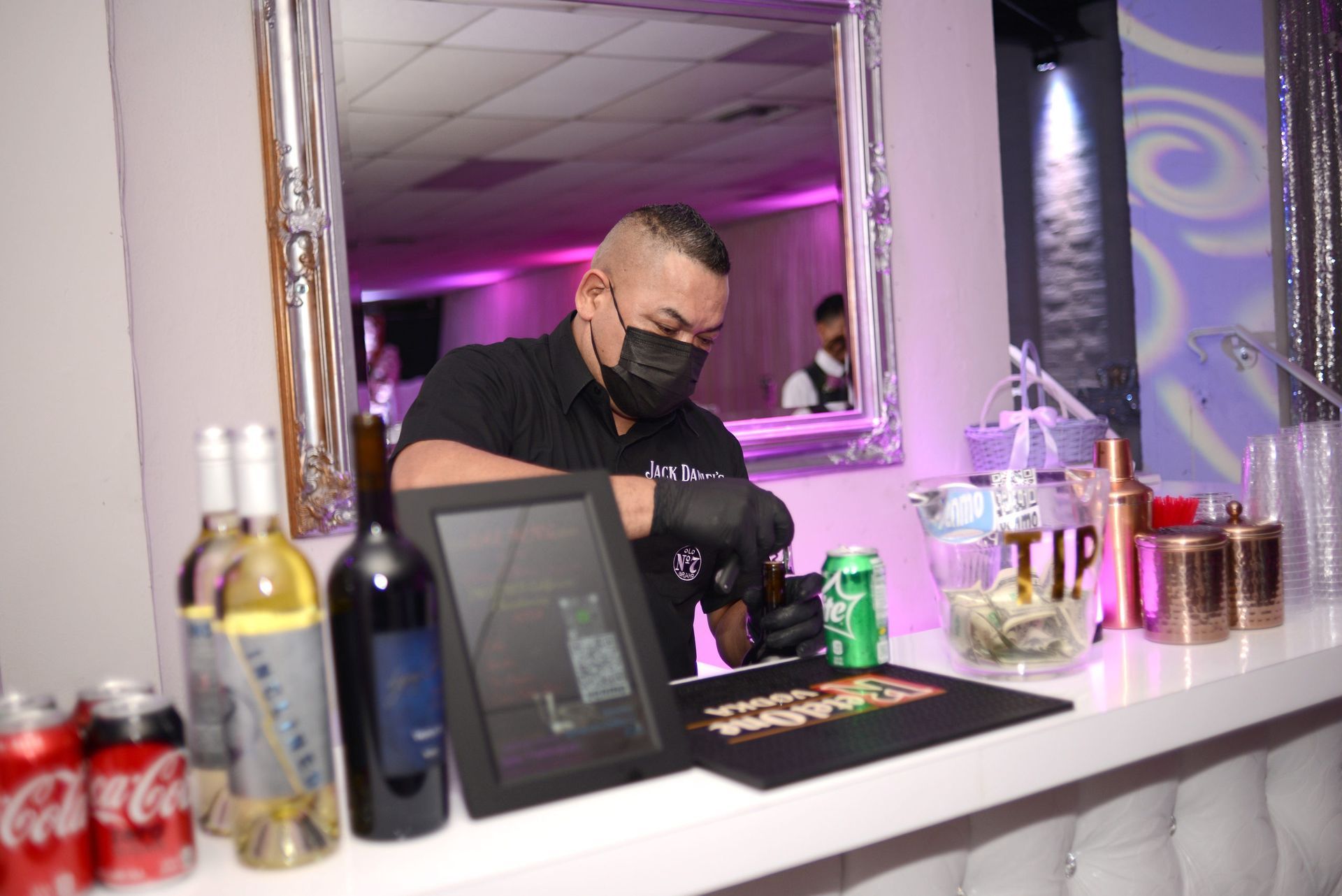 A man wearing a mask is standing behind a bar.