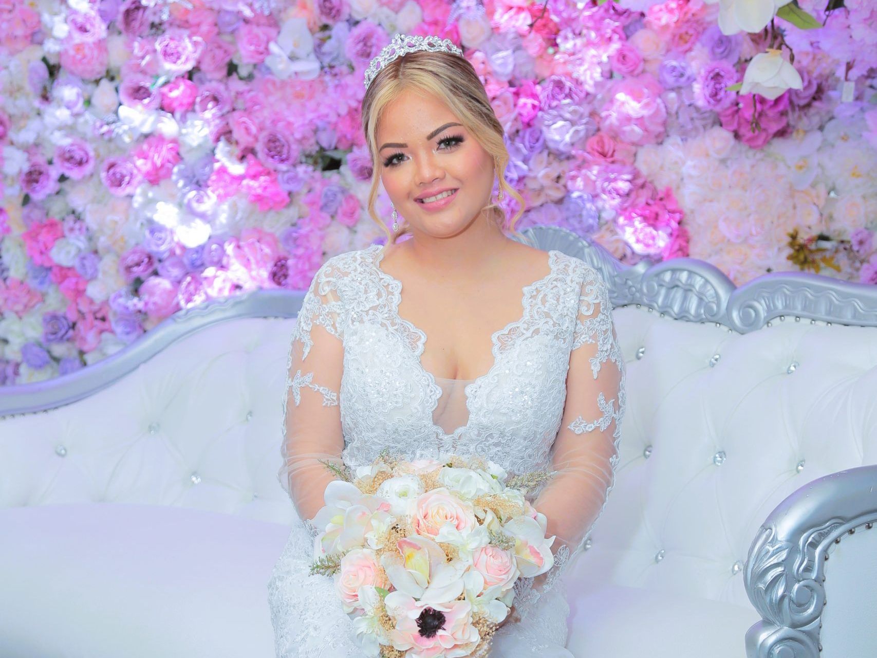 A bride in a wedding dress is sitting on a couch holding a bouquet of flowers.