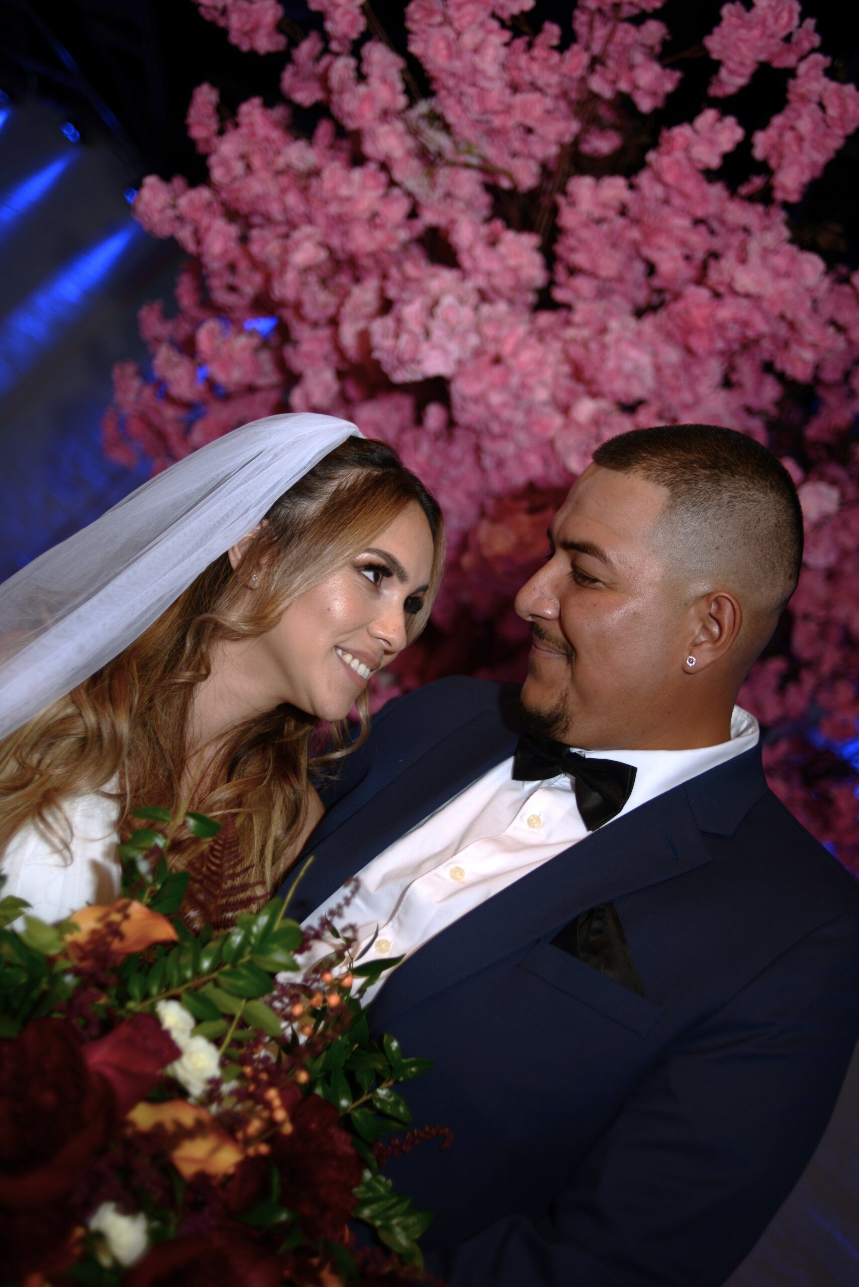 A bride and groom are posing for a picture in front of a pink cherry blossom tree.