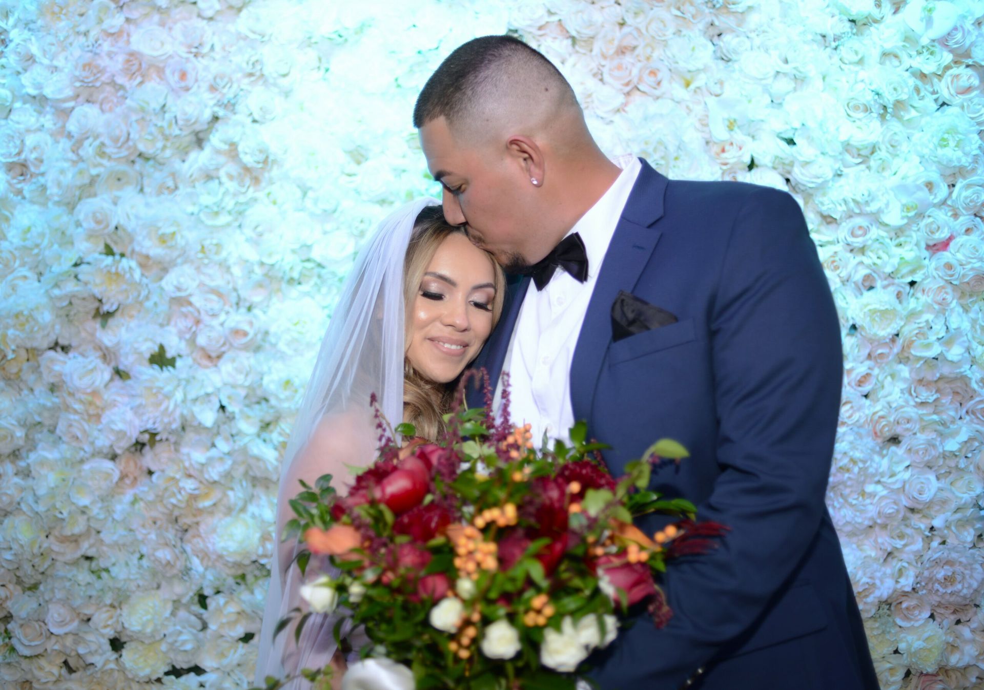 A bride and groom are posing for a picture in front of a flower wall.