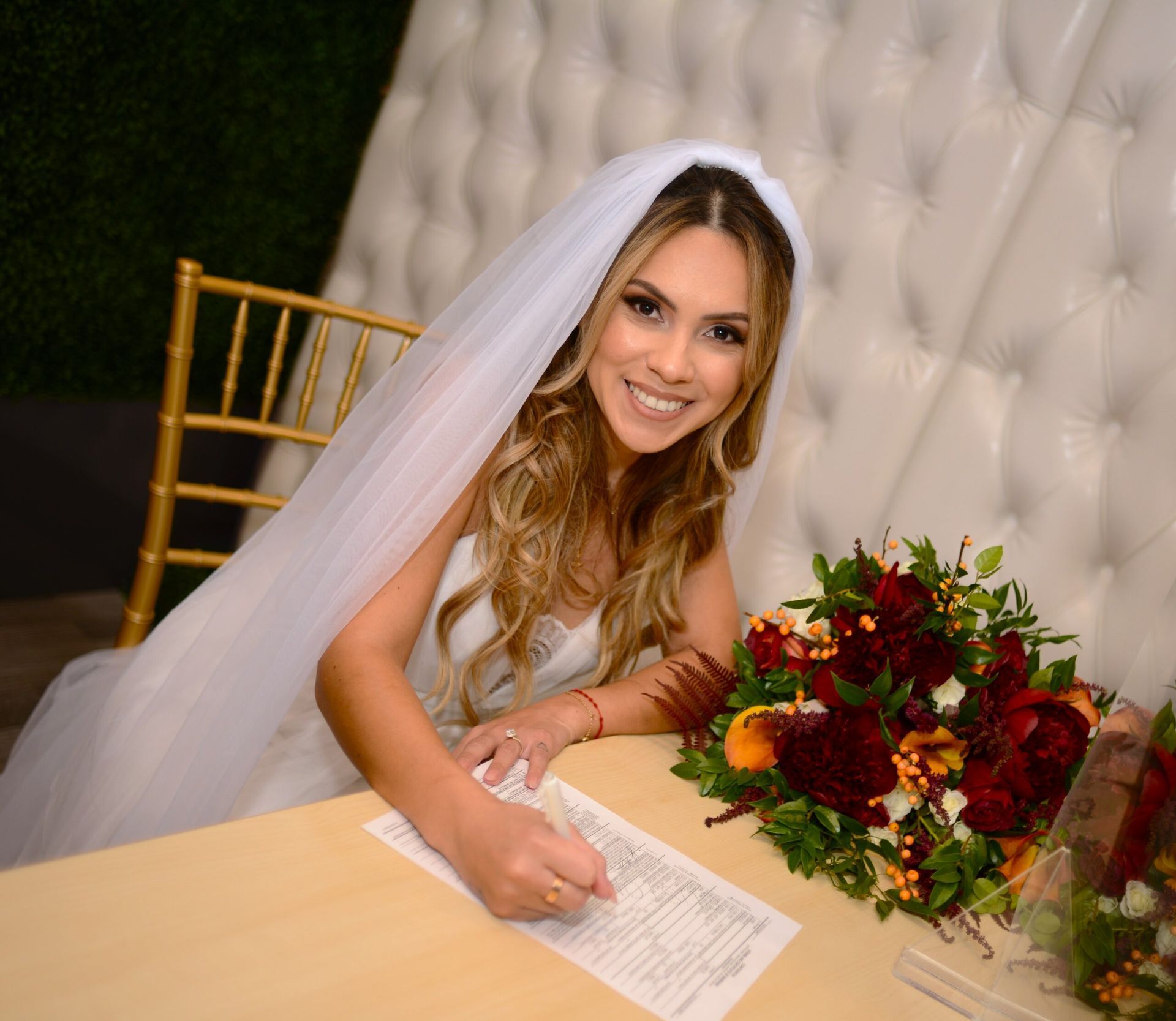 A bride is sitting at a table with a bouquet of flowers and writing on a piece of paper.