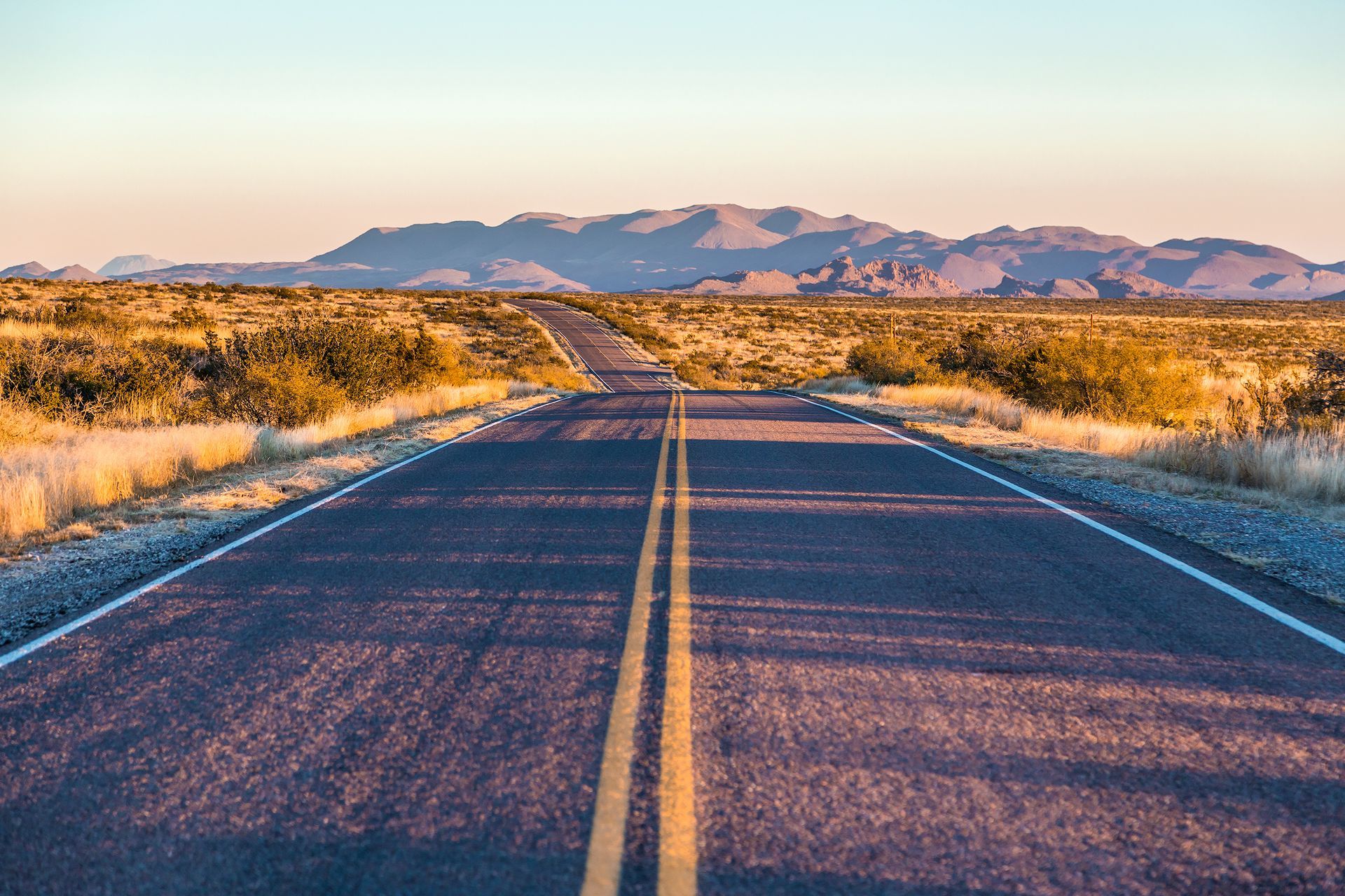 Desert road stretching towards mountains at sunset.